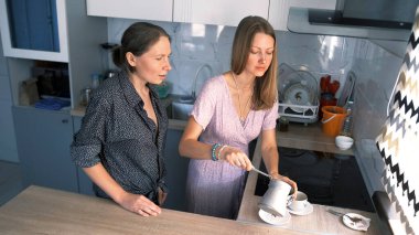 İki oda arkadaşı mutfakta durup kahve yapıyorlar. Güzel bir öğrenci arkadaşı için hindiden bir fincana kahve doldurur. Atmosfer rahat ve dost canlısı.