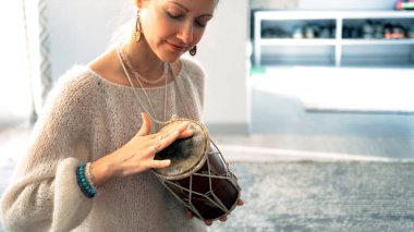 Odaklanmış genç ve güzel bir öğrenci küçük bir davulda ritmi çalıyor. Kadın gülümsüyor ve elinde bir davul tutuyor ve çalmasından ve müzikten zevk alıyor..