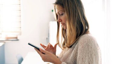 Öğrenci telefonunda bir şey arıyor. Güzel genç bir kadın bir odada duruyor ve cep telefonuna bakıyor. Kazak giyiyor ve cihazına odaklanmış durumda..