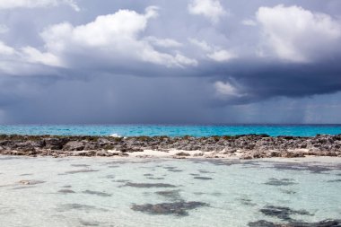 Half Moon Cay Adası 'nın kayalık plajı ve arka planda koyu yağmurlu bir gökyüzü manzarası (Bahamalar).