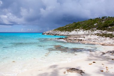 Yarım Ay Cay plajı turkuvaz renkli sular ve arka planda karanlık fırtınalı bir gökyüzü manzarası (Bahamalar)).