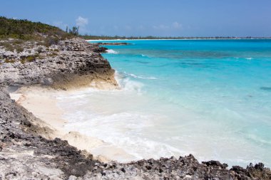 The view of turquoise color waves washing the tiny beach surrounded by rocks on Half Moon Cay island (Bahamas).