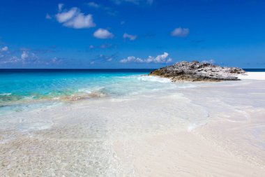 The scenic view of transparent turquoise color waters and a rock in a background on Half Moon Cay uninhabited island (Bahamas).