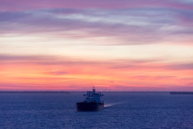 The dramatic sky over cargo ship traveling in Hillsborough Bay before the sunrise (Tampa, Florida).