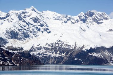 The springtime view of tall snowy mountains and calm waters in Glacier Bay national park (Alaska).