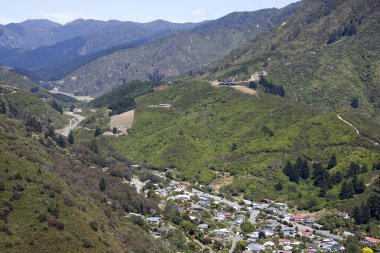 The aerial view of the ending of Picton resort town and the road leading through green mountains (New Zealand).