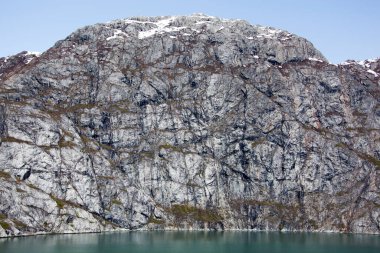 The springtime view of a steep rocky mountain with the melting snow on a top in Glacier Bay national park (Alaska).