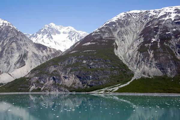 The springtime view of tall mountains and calm water with ice in Glacier Bay national park (Alaska).