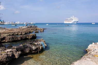 Grand Cayman adasının sabah manzarası kayalık kıyı ve arka planda sürüklenen bir yolcu gemisi.