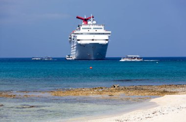 Grand Cayman Adası (Cayman Adaları) yakınlarındaki büyük yolcu gemisinin yanından geçen bir turist teknesinin manzarası.).