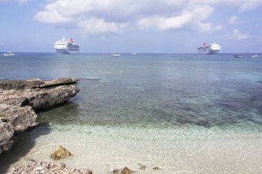 Büyük Cayman adasındaki küçük bir sahilin manzarası ve arka planda sürüklenen farklı büyüklükteki gemiler (Cayman adaları)).