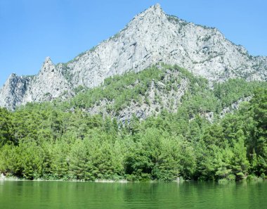 Arkasında dik bir dağ bulunan yeşil renkli Karacaoren Gölü manzarası (Antalya, Türkiye)).