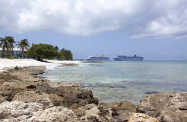 Büyük Cayman adasının manzarası bulutlu gökyüzünün altındaki Seven Mile Beach ve arka plandaki yolcu gemileri (Cayman adaları)).