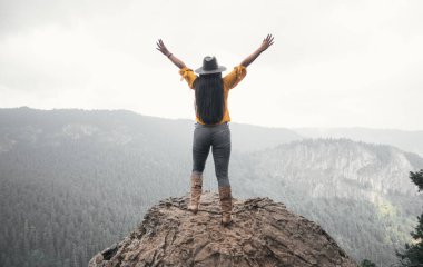 Şapkalı genç bir kadın dağ manzarasını izliyor.