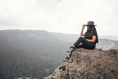 Şapkalı genç bir kadın dağ manzarasını izliyor.
