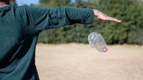 Child's hand throwing a plastic bottle in nature