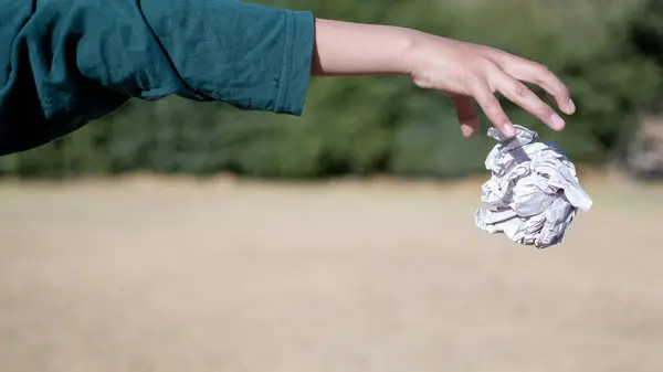 Hand throwing a paper ball in nature