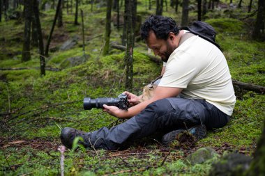 Meksikalı adam ormanda oturup fotoğraf çekiyor.