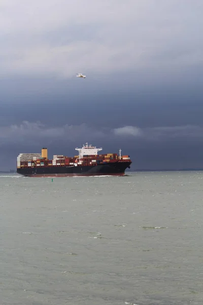 Stock image a big cargo ship is navigating at sea with stormy weather and a dark grey sky