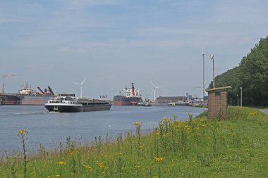 Ghent-Terneuzen Kanalı 'nın manzarası. Westerschelde' ye ve Terneuzen 'deki kuzey denizine giden iki tekne. Yazın kır çiçekleriyle dolu yeşil bir tepe boyunca ilerliyorlar.