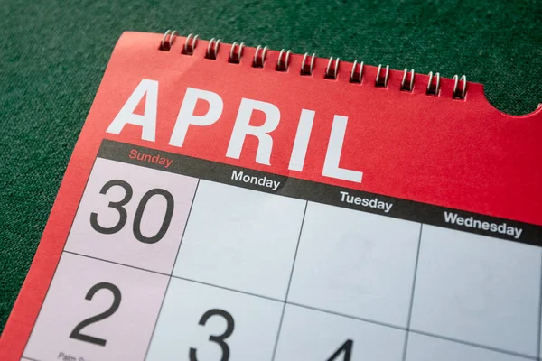 Calendar 2023, April, monthly planner. Day, month, year, date and activity organiser wall and desk planner. Red and white calendar with large letters and numbers on green background. Close up.