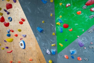 Multicoloured traverse climbing wall holds and grips of various shapes and sizes on grey and green indoor climbing wall at activity centre.