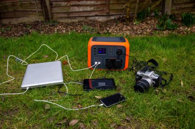 Portable power station solar electricity generator with laptop, tablet and camera electronic devices charging outdoors on garden lawn grass. Wireless charging lithium battery backup for use anywhere. clipart