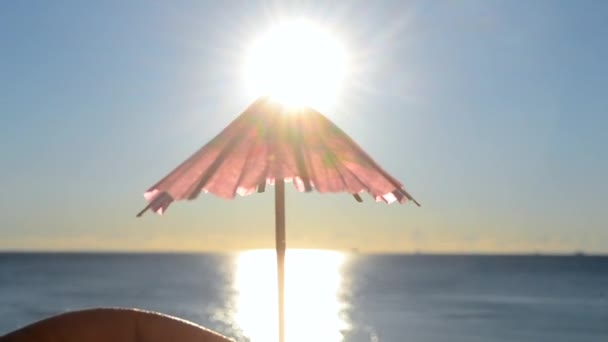 青い空を背景に 1枚の赤い紙の傘を手に持つ男は 青い海の表面に明るく輝く太陽と日当たりの良いパスをカクテル装飾 旅行観光の概念 — ストック動画