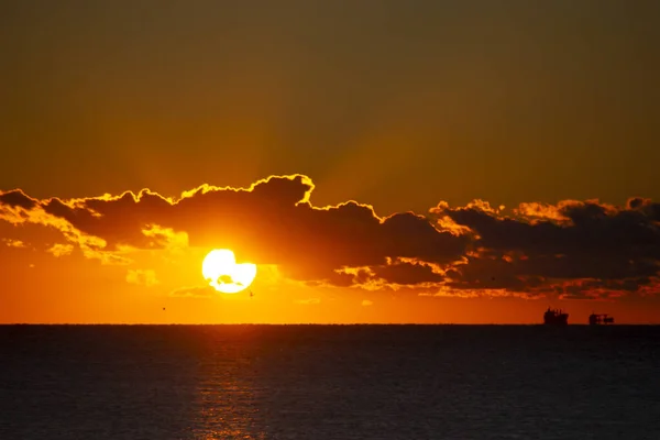Dawn sun go behind cloud over sea horizon during dawn. Sunbeams, sun rays. Dawn sunrise dawning on sea. Black silhouettes of sea and clouds. Sky sea landscape. Seascape Fast moving clouds