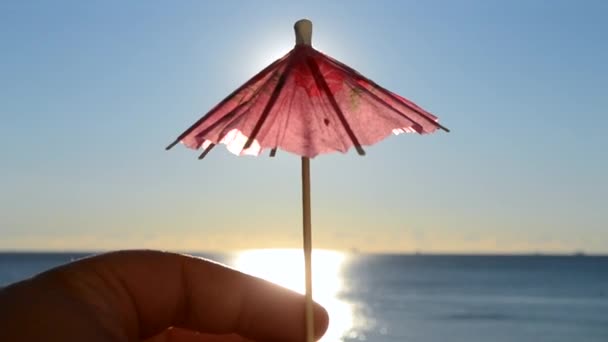 青い空を背景に 1枚の赤い紙の傘を手に持つ男は 青い海の表面に明るく輝く太陽と日当たりの良いパスをカクテル装飾 旅行観光の概念 — ストック動画
