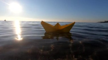 Deniz dalgalarında yüzen küçük sarı kağıt tekne, güneşli bir gün. Alt manzara, yakın plan. Temiz şeffaf su, parlak güneş, bulutsuz temiz mavi gökyüzü. Ve sualtı görüşü Seyahat rüyalarının amacı