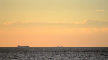 Zaman ayarlı. Denizdeki ufuk çizgisinde tanker tankerlerinin silueti ve gün batımında sarı mavi gökyüzünde hızlı hareket eden bulutlar. Deniz manzarası, deniz manzarası. Ulaşım. Doğal arkaplan