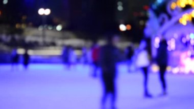 Bulanık soyut arkaplan. Birçok insan açık hava buz pateni pistinde kayıyor, kış gecesi büyük bir Noel ağacı süsledi. Noel tatili kutlanır. Bulanık renkli tatil arkaplanı