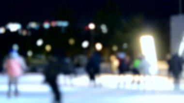 Bulanık soyut arkaplan. Birçok insan kış gecesi açık hava buz pateni pistinde paten kayıyor. Noel tatili kutlanır. Bulanık renkli tatil arkaplanı