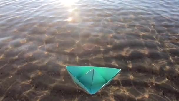 晴れた日には透明な水と砂の底で海の波に揺れる小さな緑の紙のボート 折り紙船が接近中 夢のような旅行の概念 — ストック動画