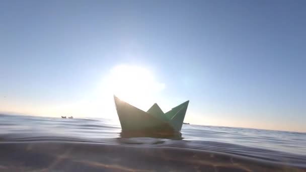 小さな緑の紙のボートの海の波 晴れた日に浮かんでいる 下のビューでは クローズアップ 透明な水 明るく輝く太陽 雲のないきれいな青い空 そして水中ビューコンセプト旅行夢の目標 — ストック動画