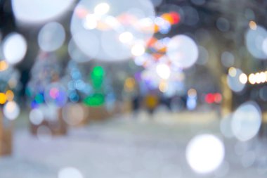 Arka plan bulanık. Kış gecesi kar yağarken şehir caddesi. Birçok süslü Noel ağacı, aydınlanma, sokakta süsleme. Yılbaşı bayramı kutlaması. Ağaçlardaki fenerler