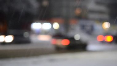 Arka plan bulanık. Kış gecesi kar yağışında arabalar şehirde yol boyunca sürüyorlar. Bulanık bokeh noktaları. Sokak lambaları, fenerler, parlak farlar. Kış manzarası. Doku arkaplanı.