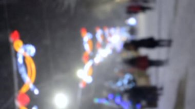 Arka plan bulanık. Kentte sokakta yürüyen pek çok insan, kış gecelerinde yoğun kar yağışında yılbaşı süsleri ile süslenip süslenmişti. Yılbaşı arkaplanı. Dikey video