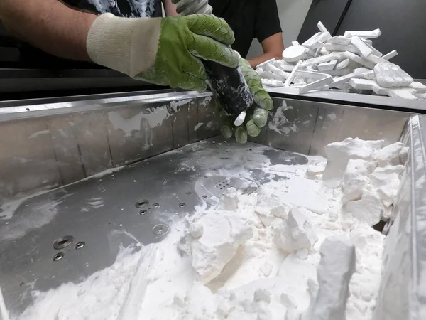 A man working with a working vacuum cleaner to clean the white powder of polyamide from a model printed on a 3D printer inside a 3D printer. Cleaning objects printed on an industrial powder 3D printer