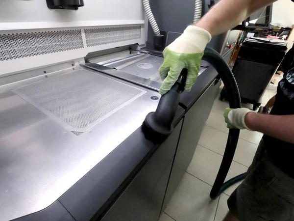 A male worker cleans the surface of an industrial 3D printer from white powder with a vacuum cleaner close-up. Multi Jet Fusion MJF 3D printing. The working process