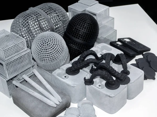 Many different models printed on 3D printer. Gray and black objects printed on 3D printer made of plastic close-up. Lots of 3D printed models. Prototypes of various shapes made by 3d printer on table.