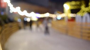 Arka plan bulanık. Birçok insan kış akşamı şehirde açık havada buz pateni pistinde kayıyor, parlak tatil çelenkleri takıyor. Noel Yeni Yıl kutlamaları Tatil eğlence arkaplanı
