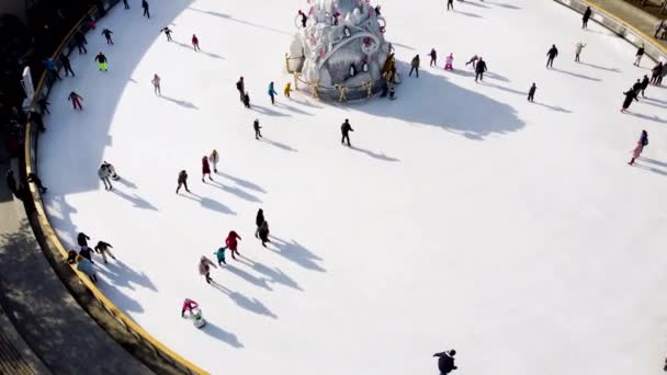 在阳光明媚的冬日 人们在户外溜冰场上滑冰 和许多人一起在溜冰场上空飞舞 很长的阴影公共城市冰场 顶部视图 空中无人驾驶飞机视图 — 图库视频影像
