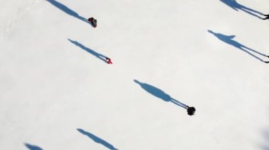 Üst görünümü özetle. Uzun gölgeleri olan insanlar güneşli kış günlerinde beyaz buz pateni pistinde kayıyorlar. Halka açık buz pateni pisti. Hava aracı görüntüsü. Eğlence sporları tatili