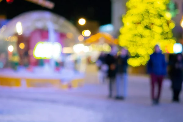 Stock image Blurred background. Christmas tree, decorated glowing lights, building, blurry silhouettes of people walking city square at winter night. Beautiful New Year and Christmas holiday blurred background