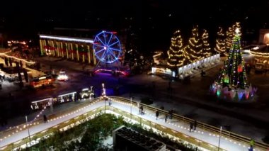 Birçok insan açık havada buz pateni pistinde paten kayıyor. Yılbaşı süsleri, süslemeler, kış gecelerinde parlak çelenkler. Yeni yıl Noel kutlaması. Havadan
