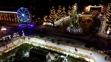 Birçok insan açık havada buz pateni pistinde paten kayıyor. Yılbaşı süsleri, süslemeler, kış gecelerinde parlak çelenkler. Yeni yıl Noel kutlaması. Havadan