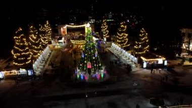 Birçok insan açık havada buz pateni pistinde paten kayıyor. Yılbaşı süsleri, süslemeler, kış gecelerinde parlak çelenkler. Yeni yıl Noel kutlaması. Havadan