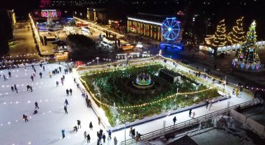 Birçok insan açık havada buz pateni pistinde paten kayıyor. Yılbaşı süsleri, süslemeler, kış gecelerinde parlak çelenkler. Yeni yıl Noel kutlaması. Havadan